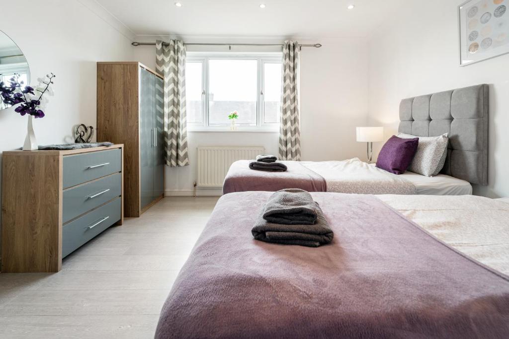 伦敦Dwellers Delight Living Ltd Serviced Accommodation, Chigwell, London 3 bedroom House, Upto 7 Guests, Free Wifi & Parking的一间卧室配有两张床和一个带毛巾的梳妆台。