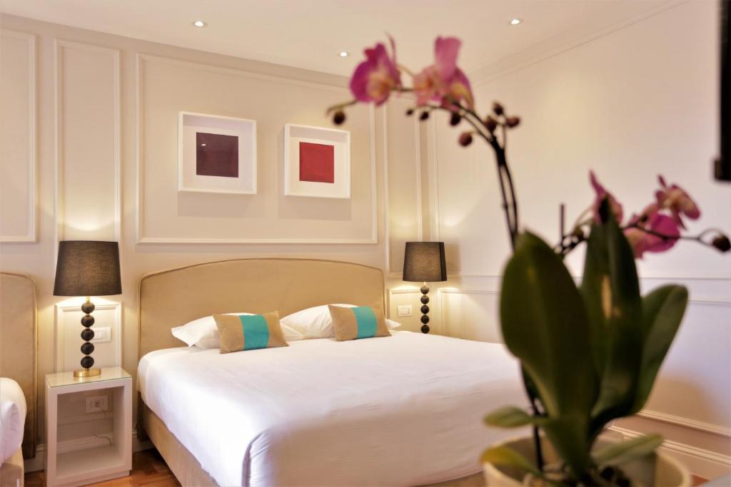 钱皮诺别墅套房酒店的一间卧室配有床和种有粉红色花卉的植物