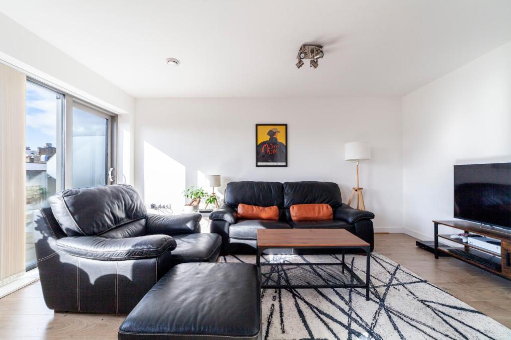 伦敦Contemporary Top floor flat in Kentish Town的客厅配有黑色真皮沙发和电视
