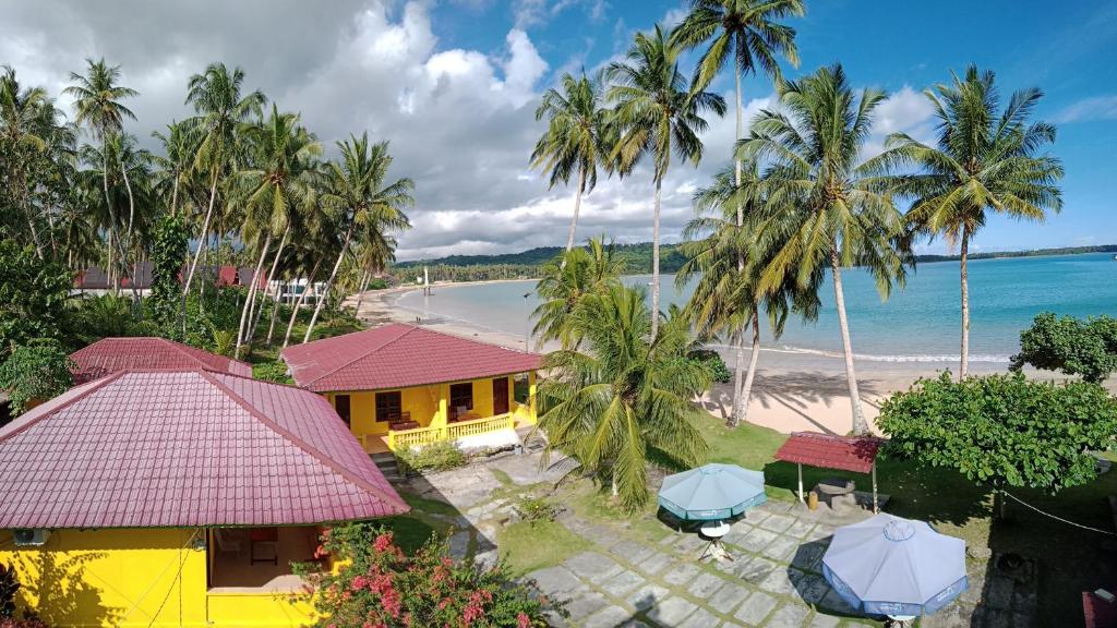 LagudriHarus Damai Inn的享有海滩的空中景致,拥有黄色的房屋和棕榈树