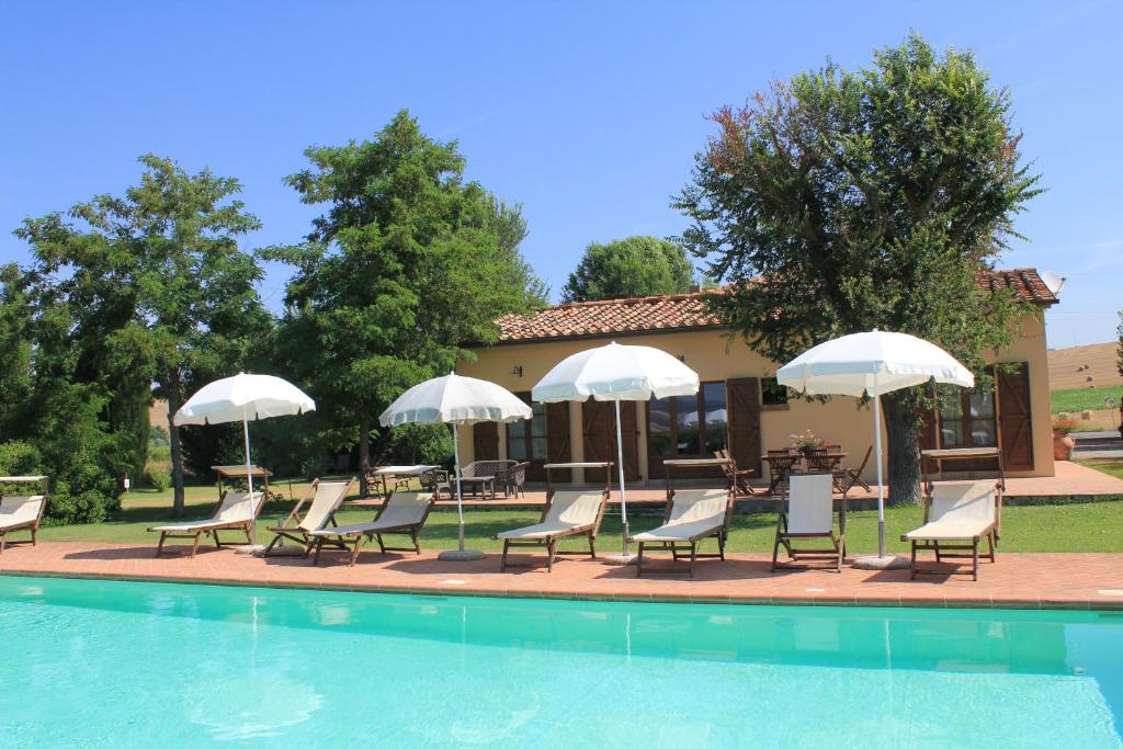 皮恩扎Agriturismo Piandimaggio的一组椅子和遮阳伞,位于游泳池旁
