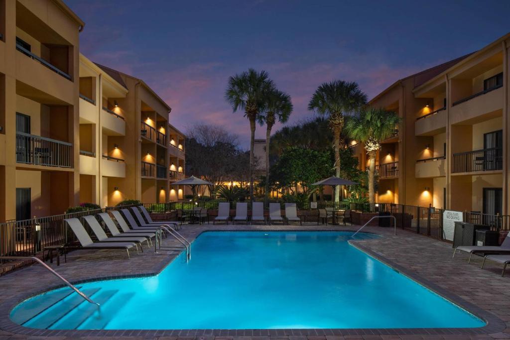 杰克逊维尔Courtyard by Marriott Jacksonville at the Mayo Clinic Campus/Beaches的夜间游泳池,带椅子,酒店