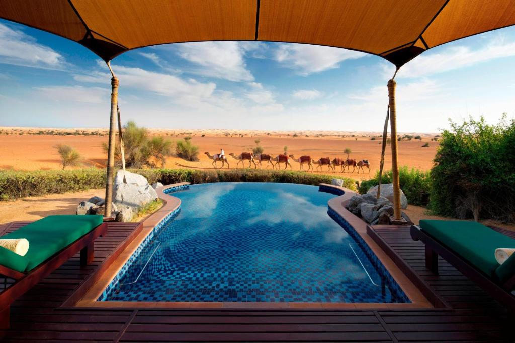 Murquab迪拜阿玛哈豪华精选沙漠水疗度假酒店的享有沙漠景色的游泳池,有一群马