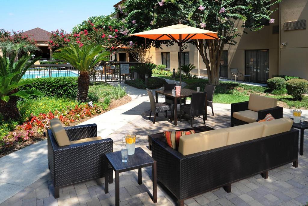 休斯顿Courtyard by Marriott Houston Hobby Airport的一个带沙发和桌子及遮阳伞的庭院