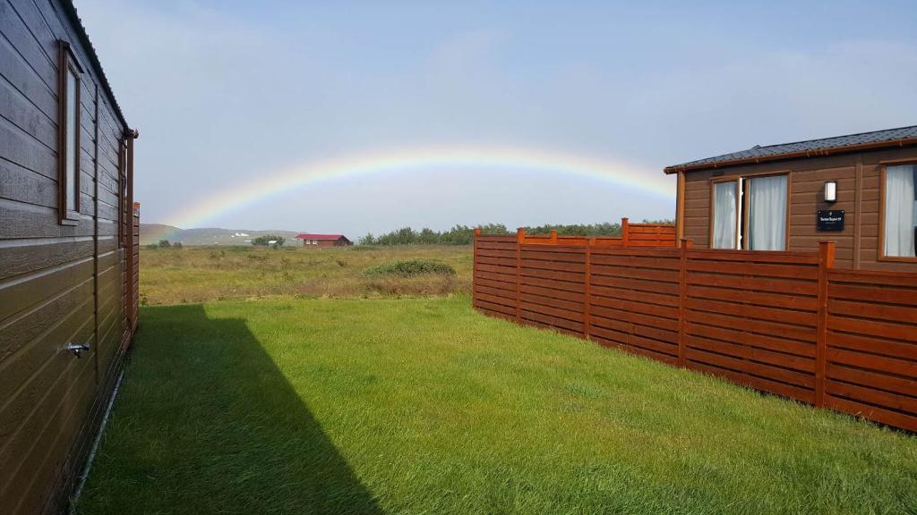 SkagaströndStuðlaberg的彩虹在有栅栏和房子的田野上
