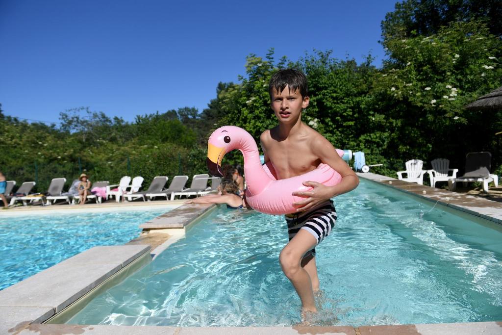 莱塞齐耶德泰阿克Camping Le Pech Charmant的一个在游泳池里拿着粉红色火烈鸟的男孩