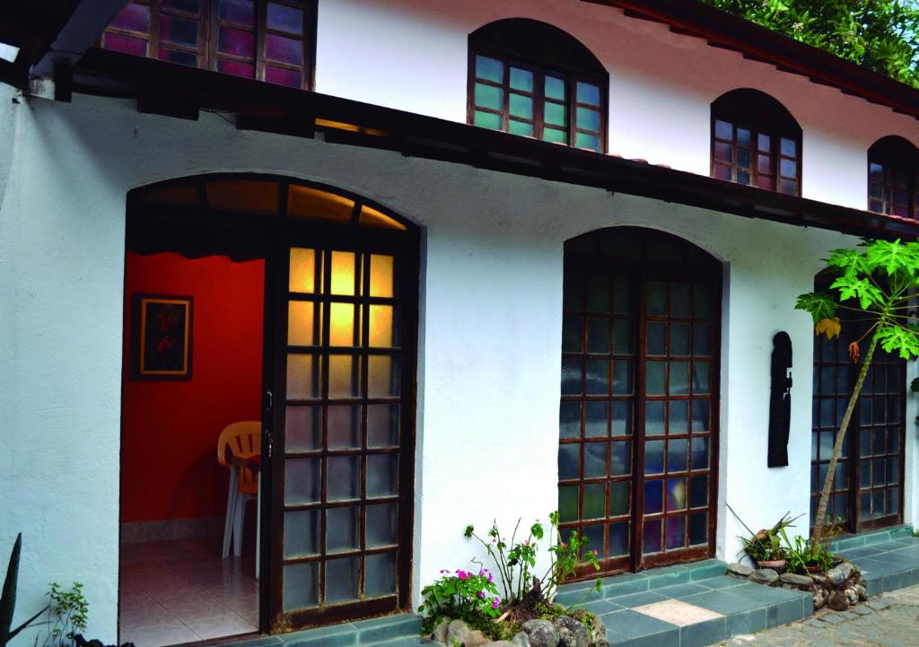 特林达德Pousada Em Busca do Sol的白色的房子,有红色的门和窗户