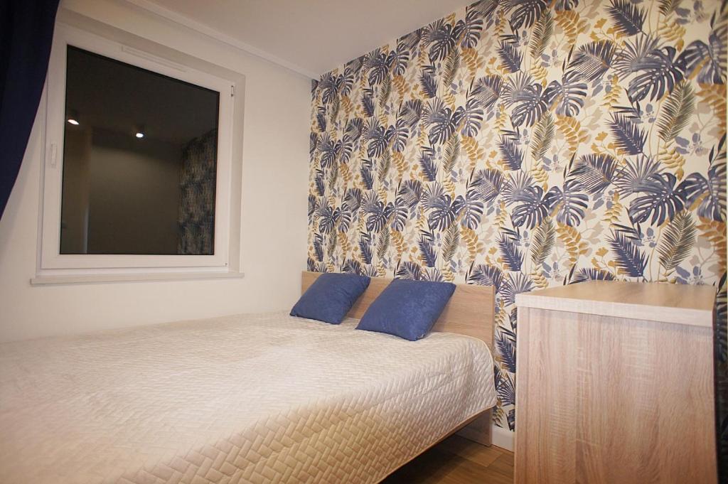 绿山城Drzewna Apartamenty -Augustowska的一间卧室配有一张带蓝色枕头的床和壁纸