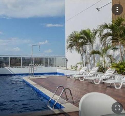 马瑙斯#SENSACIONAL# PREMIUM HOTEL Manaus AM的一座带白色椅子和棕榈树的游泳池