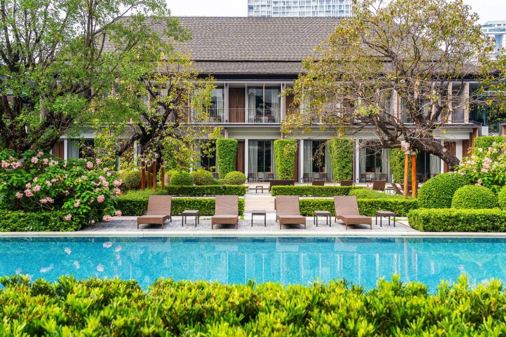 曼谷Villa Deva Resort & Hotel Bangkok的一座带椅子和植物的建筑前的游泳池