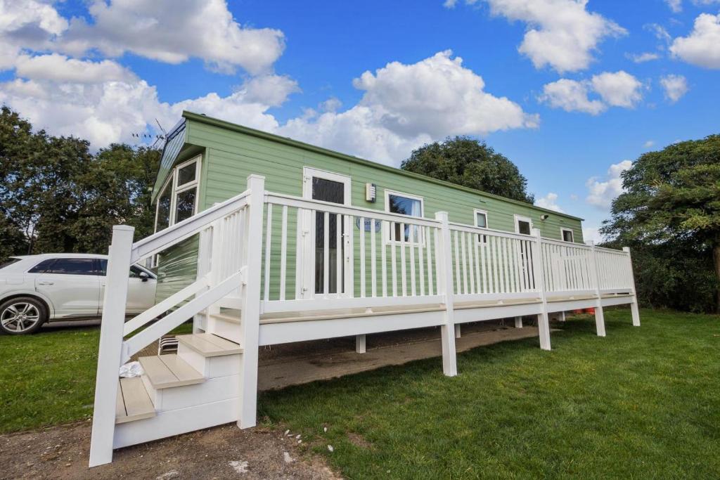 滨海克拉克顿Great 8 Berth Caravan For A Staycation In Clacton-on-sea Ref 26436e的绿色房子,设有白色门廊和汽车