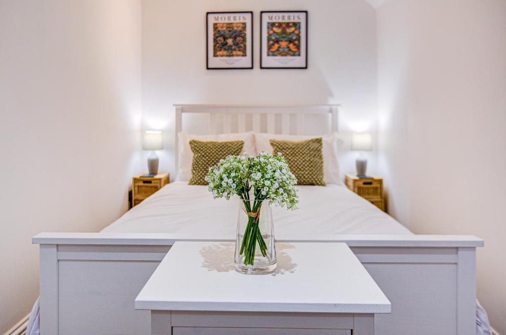布伦特伍德Beautiful One Bedroom Apartment的一张白色的床,桌子上放着花瓶
