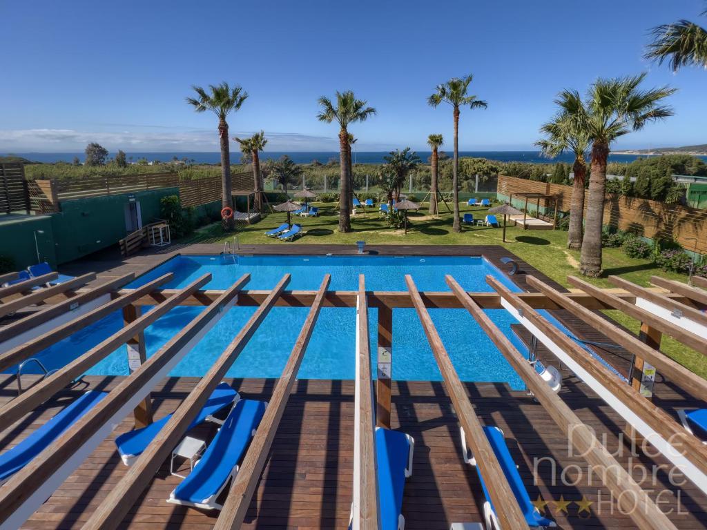 塔里法Dulce Nombre Tarifa的一个游泳池的形象,游泳池里摆放着蓝色的椅子和棕榈树