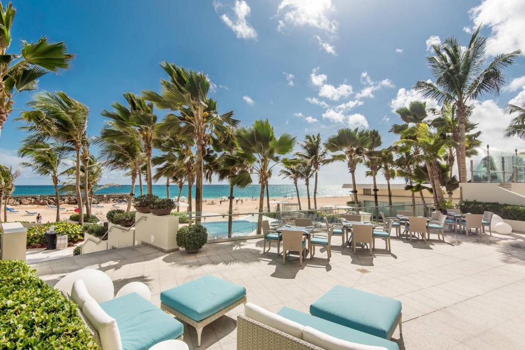 圣胡安圣胡安孔查万丽酒店的海滩上的露台,配有桌椅和棕榈树