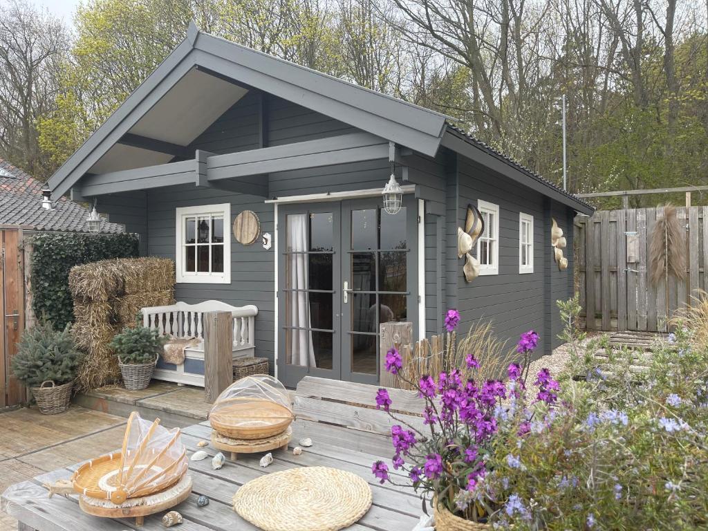 诺德韦克Cabin De Duinweg: direct aan duin en bos的一个小灰色的棚子,带野餐桌和鲜花