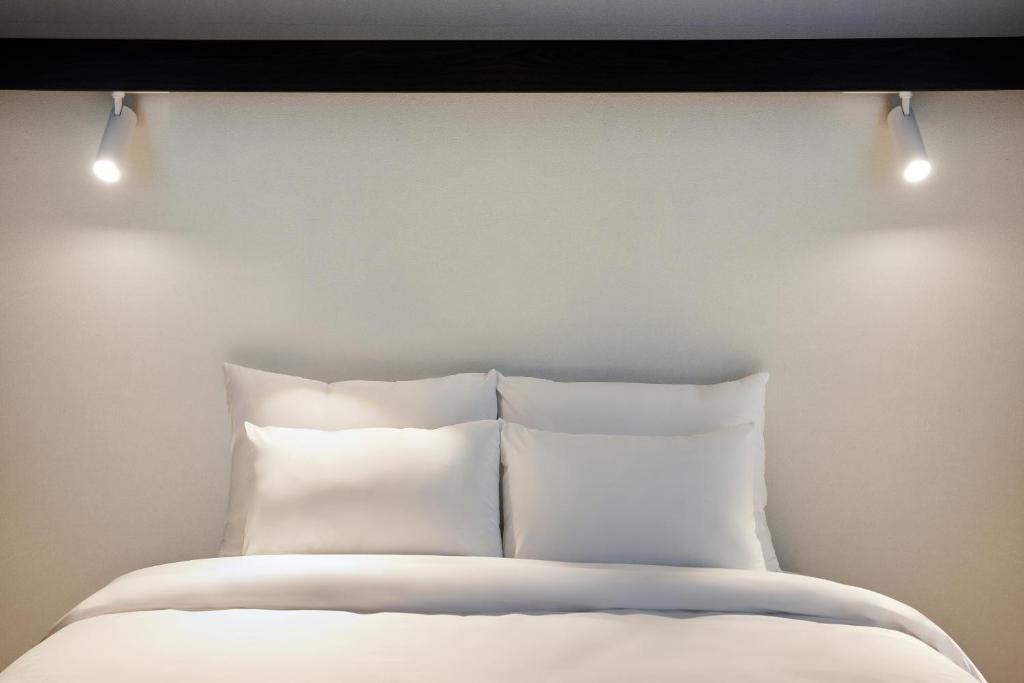 首尔The Connoisseur Residence Hotel的床上方设有白色枕头和灯