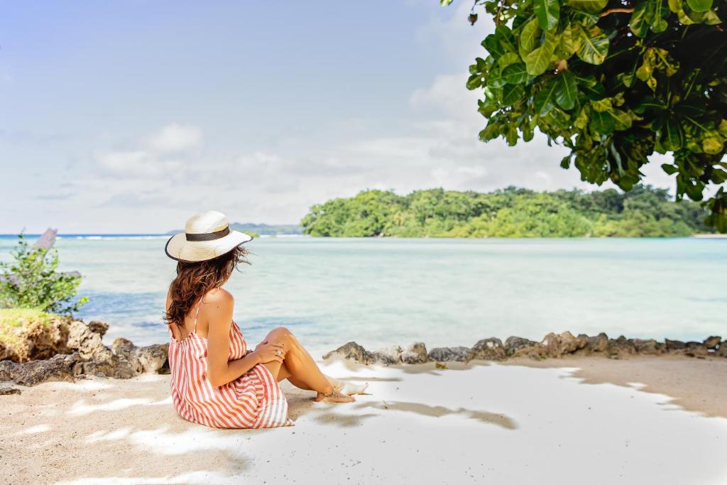 卢甘维尔海龟湾酒店 的坐在海滩上的女人,穿着条纹的衣服和帽子