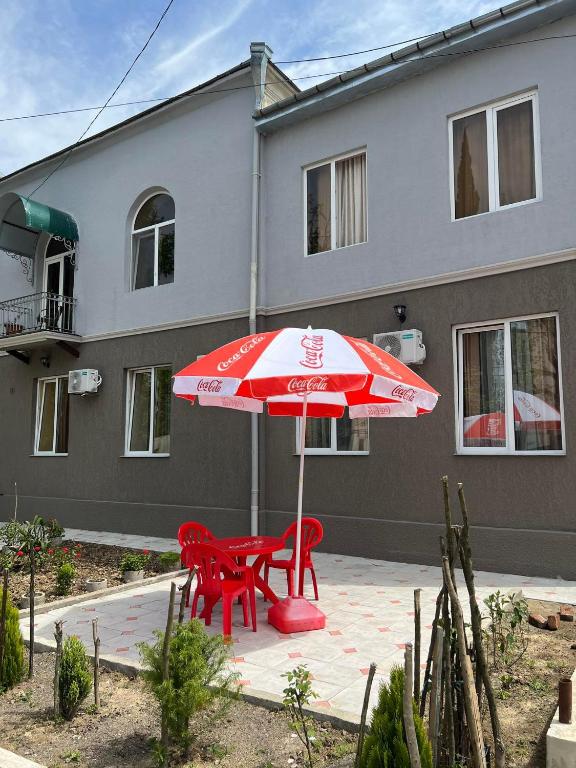 茨卡尔图博Guest House Kolkha的房子前的一把雨伞下的红色桌子和椅子