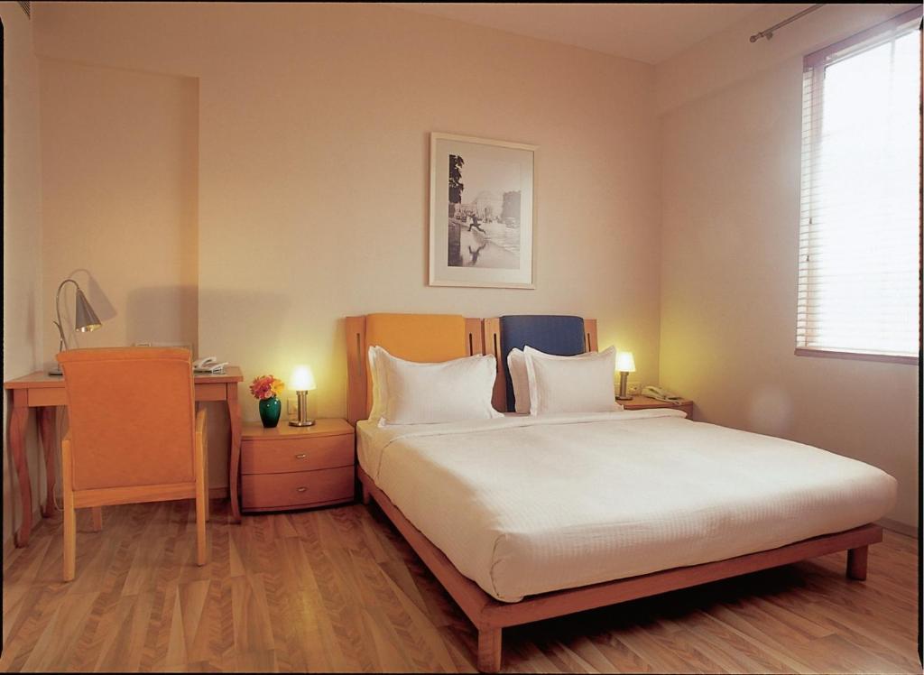 孟买The Gordon House Hotel, Colaba的一间卧室配有一张床、一张书桌和一个窗户。