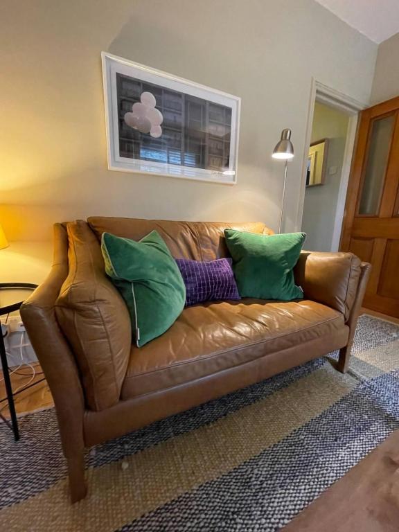 伦敦Beautiful & Cosy 2BD House - Southwark的棕色皮沙发,配有绿色和紫色枕头