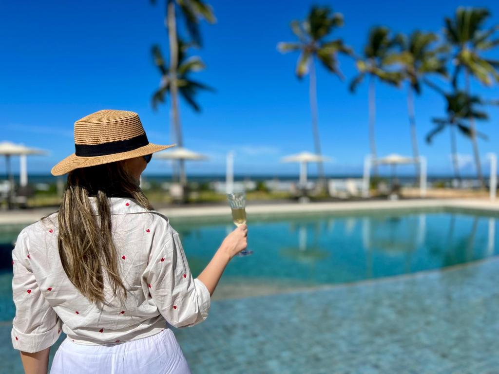伊列乌斯Kalug - Duplex PÉ NA AREIA com 4 suítes, piscina e churrasqueira privativa na Praia do Sul! Perfeito para família - Wifi 300mb!的一位在游泳池附近拿着一杯香槟的女人