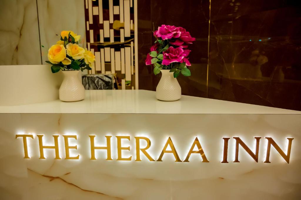 门格洛尔Hotel Heraa International的两个花瓶,花在桌子上,有 ⁇ 的标志