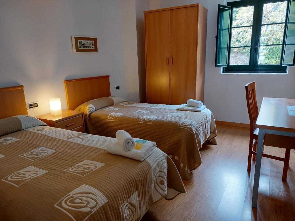 萨莫斯Hospedería Externa del Monasterio的酒店客房设有两张床、一张桌子和一张书桌。