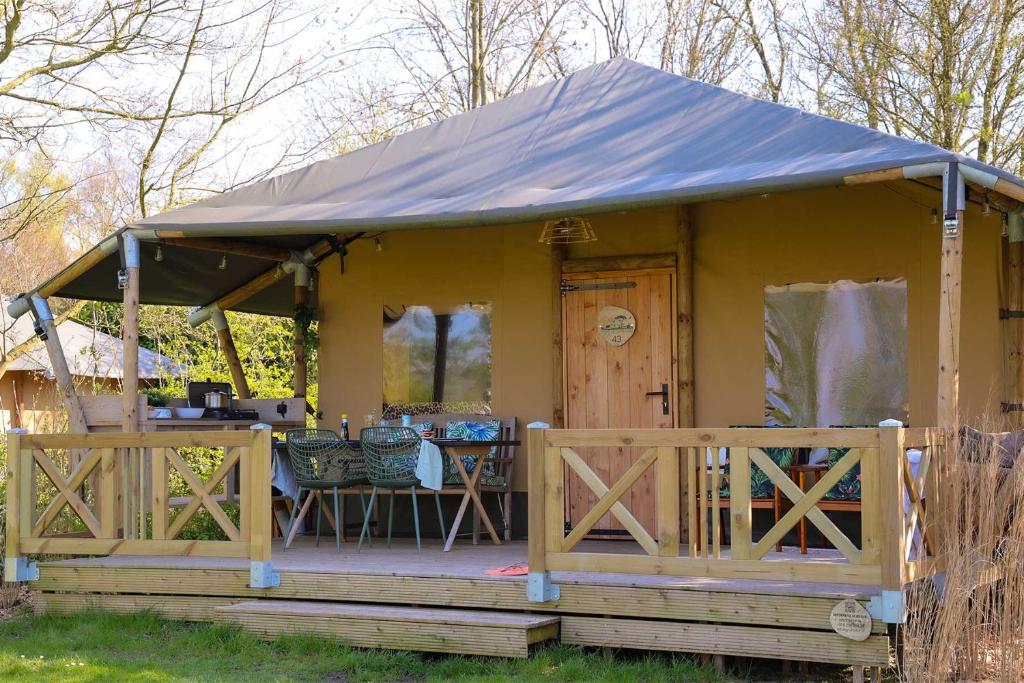 赫劳Glamping Safarilodge 'Grutte Fiif' met airco, extra keuken op veranda en privé achtertuin的黄色的小房子,设有门廊和桌子