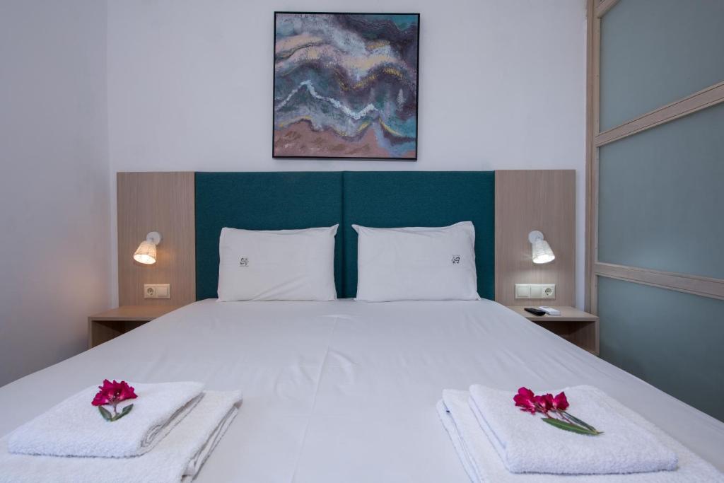 埃拉福尼西岛Elafonisi Village的卧室配有白色大床,毛巾上摆放着红色鲜花