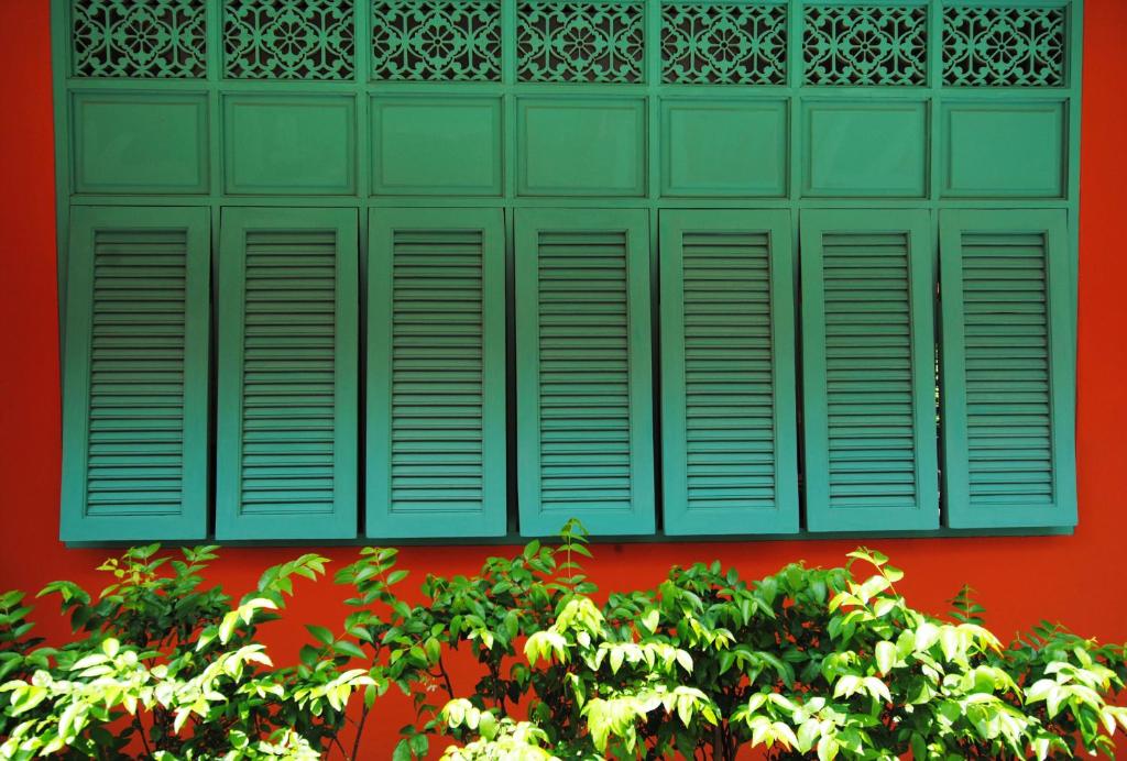 曼谷佛卡尔本地住宿加早餐酒店的红墙上的绿色窗户,灌木丛