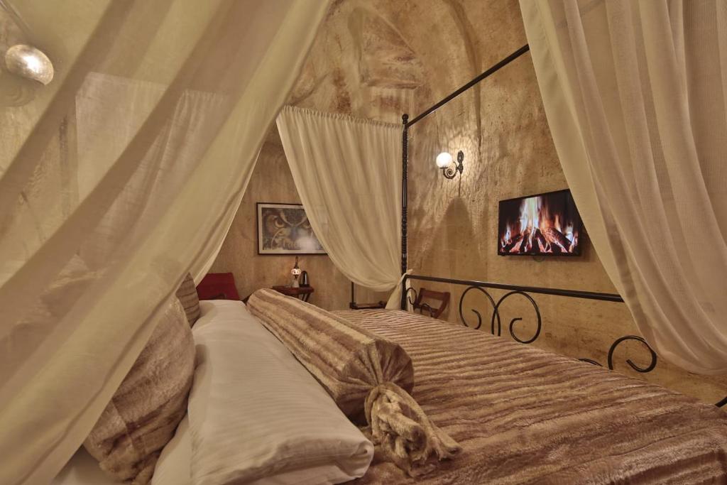 于尔居普卡帕多西亚阿苏瓦里套房酒店的一间卧室设有一张天蓬床,墙上配有电视。
