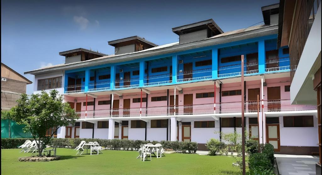 斯利那加hotel new sahil的一座粉红色和蓝色的建筑,在院子里设有白色的椅子