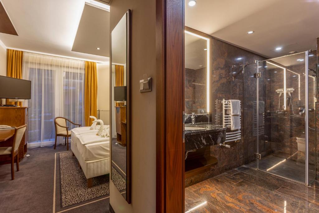 布达佩斯佐尼依花园酒店的一间带玻璃淋浴间的浴室和一间卧室
