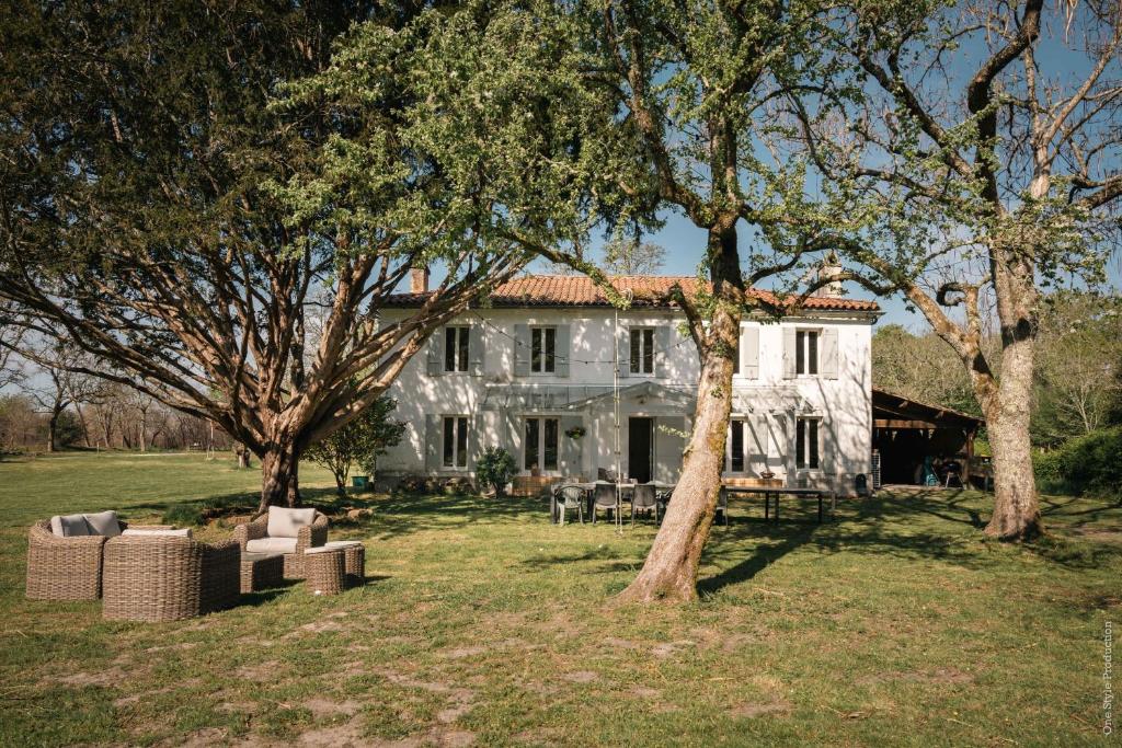 HostensEntre Chênes et Pins - Gîte de groupe 3 étoiles的前面有树木的白色房子