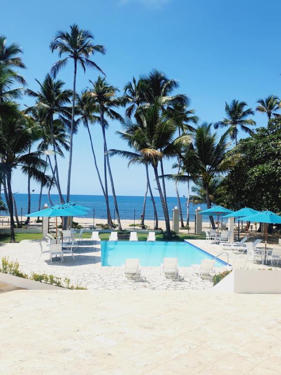 璜多里奥3 bedroom, front of the beach and pool的海滩上的游泳池,种植了棕榈树,配有蓝色遮阳伞