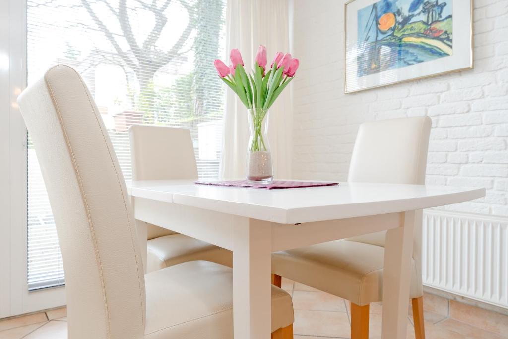 蒂门多弗施特兰德Haus Eva Mar am Meer Appartement 7的白色的餐桌,配有椅子和一束粉红色的花瓶
