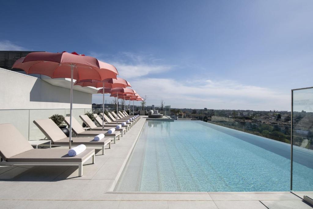 波尔图Renaissance Porto Lapa Hotel的一座大楼内的游泳池,配有椅子和遮阳伞