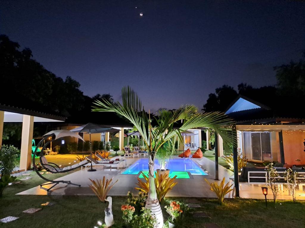 Ban ChamrungPool Villa, Resort, Mae Ramphueng Beach, Ban Phe, Rayong, Residence M Thailand的一座晚上在院子里种棕榈树的游泳池