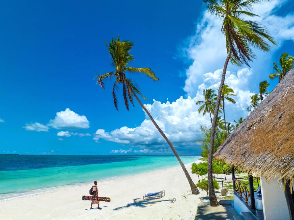 乌罗阿F-Zeen Boutique Hotel Zanzibar的一个人在海滩上散步,那里有长凳和棕榈树