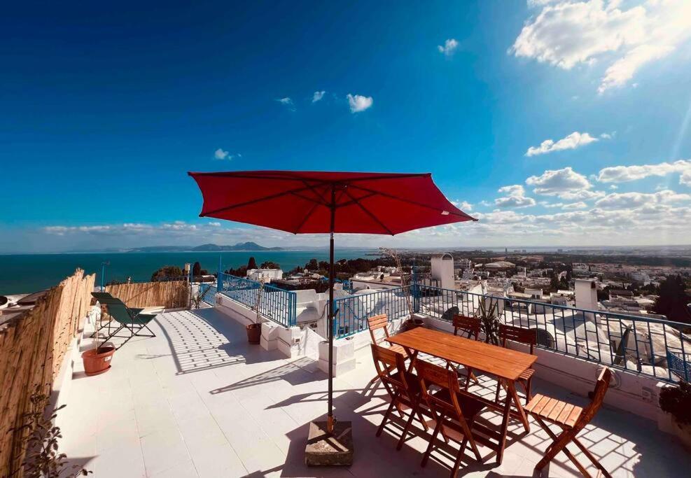 西迪·布·赛义德The Blue Sea View Sidi Bou Said的阳台配有桌椅和红色遮阳伞