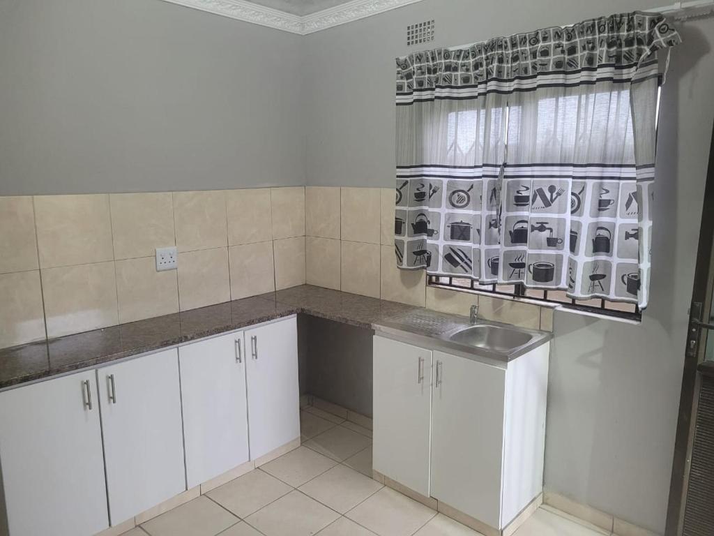 恩潘盖尼Mavundla lifestyle lodge的厨房配有白色橱柜、水槽和窗户。