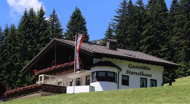米特尔贝格Gasthof Starzelhaus的山丘上的房子,前面有旗帜