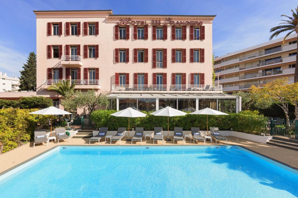 戛纳The Originals Boutique, Hôtel des Orangers, Cannes (Inter-Hotel)的大楼前的带椅子和遮阳伞的游泳池