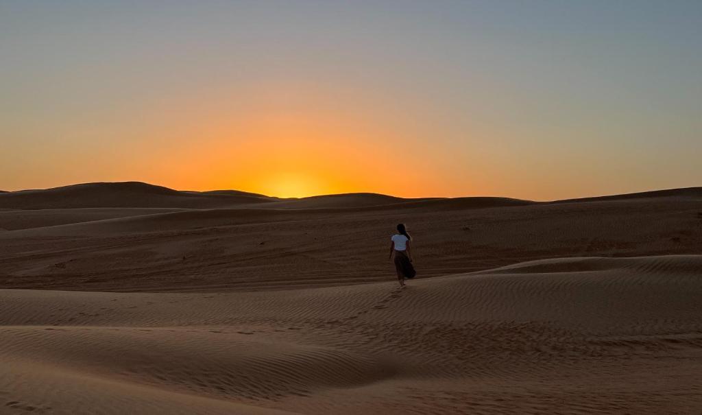 Al WāşilDelight Desert Camp的日落时在沙漠中行走的女人