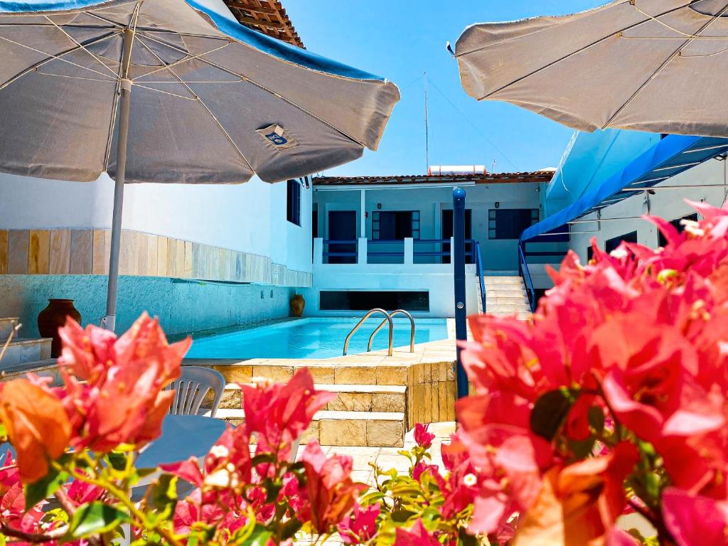阿拉卡茹Pousada Villa Grécia的一个带遮阳伞和一些粉红色鲜花的游泳池