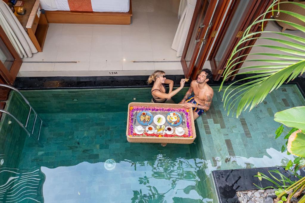 勒吉安Seminyak Sanctuary Villa by Ini Vie Hospitality的两个人坐在游泳池里,水里拿着一个手提箱