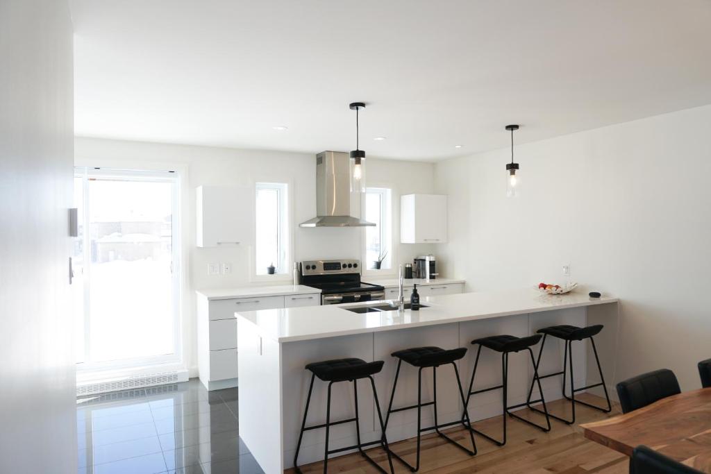 魁北克市Le Citadin - Maison neuve moderne & ensoleillée的厨房配有白色柜台和酒吧凳