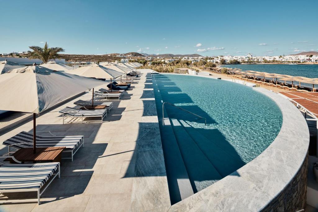 纳乌萨考斯米提斯酒店的水边带椅子和遮阳伞的游泳池