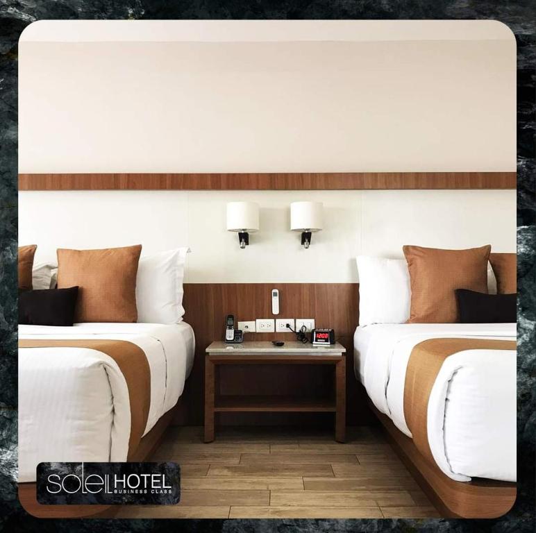莱昂Hotel Soleil Business Class的两张床铺位于一个房间,中间有桌子