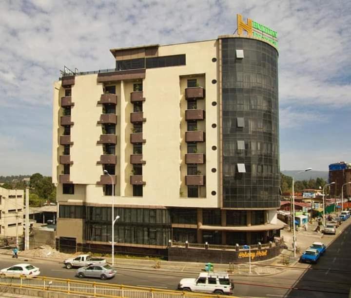 亚的斯亚贝巴Holiday Hotel Addis Ababa的一座大型建筑,前面有汽车停放